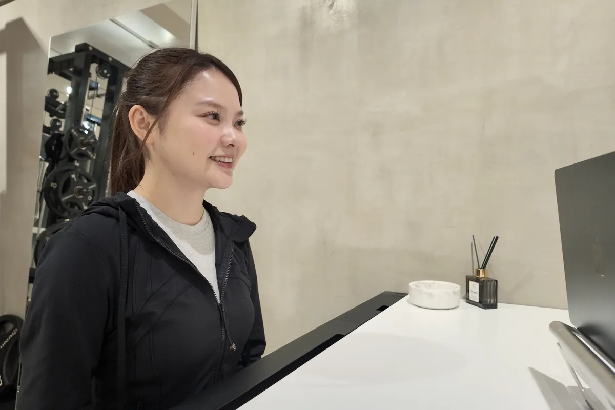 受付カウンターの前で、笑顔で話を聞くお客様｜パーソナルジムnoll-ett渋谷店