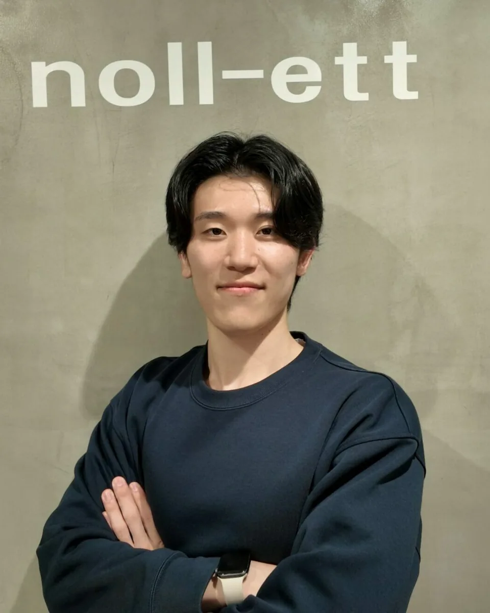 noll-ettのロゴの前で腕を組む佐藤秀紀トレーナー｜パーソナルジムnoll-ett渋谷店